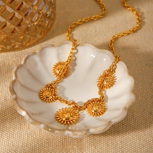 Gold stainless steel necklace with multiple sun face pendants on a white shell tray