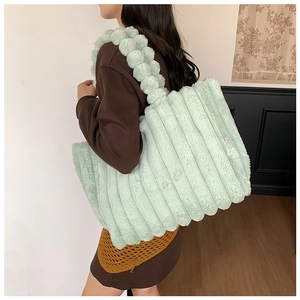 Close-up of a mint green plush tote bag with striped texture worn over the shoulder