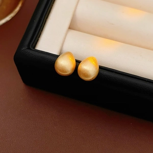 Close-up of golden teardrop stud earrings with brushed matte finish on a jewelry box