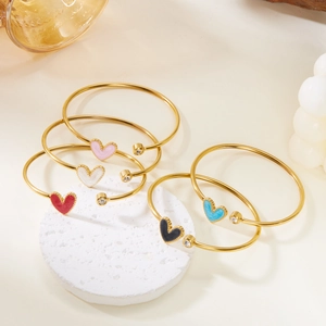 Detail of colorful enamel heart bangles with single zircon stones on textured stone base
