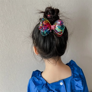 Sparkly multi-colored sequin bow hair clip for girls worn on a neat bun hairstyle