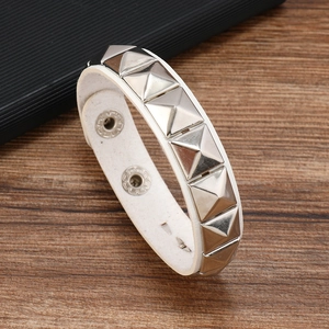 Macro shot of white leather bracelet featuring silver pyramid studs on wood surface