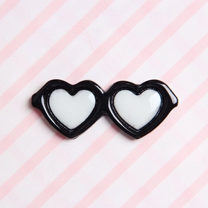 Detail view of heart-shaped mini sunglasses hair clip on a pink and white striped background