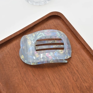 Detail showing iridescent blue acetate hair claw clip on dark wooden tray display