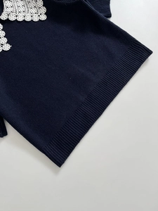 Detail of navy knit sweater featuring delicate white floral lace trim on the lapel collar