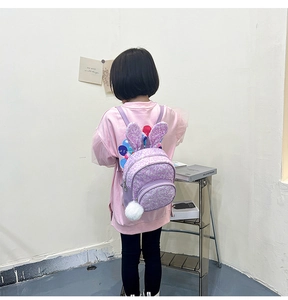Girl wearing a purple sequin backpack with bunny ears and white pompom on a simple background