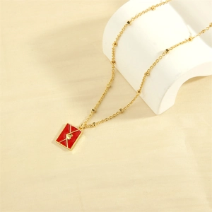 Detail of red enamel envelope pendant with gold heart on soft beige silk background