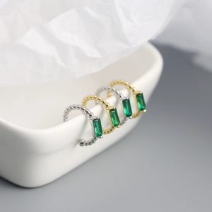 Macro shot of silver and gold bead-textured ear cuffs with rectangular emerald zircons