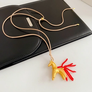 Détail d'un pendentif cheval doré avec queue en perles rouges sur cordon beige