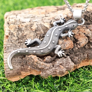 Gros plan détaillé du pendentif gecko argenté sur une texture d'écorce et d'herbe