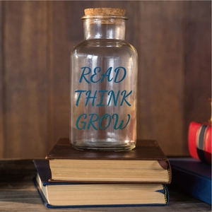 Close-up of a glass jar with cork lid featuring blue READ THINK GROW text on vintage books