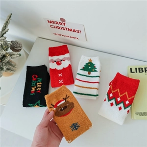 Détail de chaussettes de Noël en polaire corail aux motifs festifs sur une table blanche
