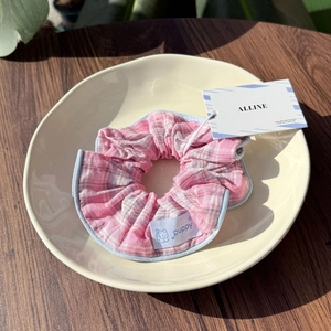 Close-up of pink plaid scrunchie with light blue trim and puppy label in a ceramic dish