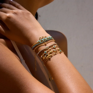 Detail of layered gold bracelets with blue gemstone, star, moon, and evil eye charms