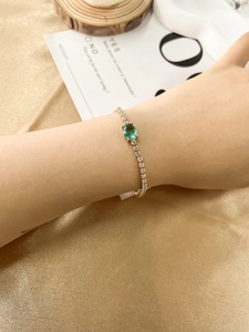 Close-up of a gold bracelet featuring a green oval gemstone and pavé zircon stones
