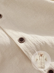 Détail de la texture en coton lin beige et boutons vintage sur la chemise à capuche