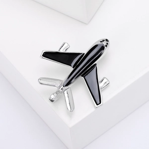Close-up of silver airplane brooch with black enamel inlay on a white surface