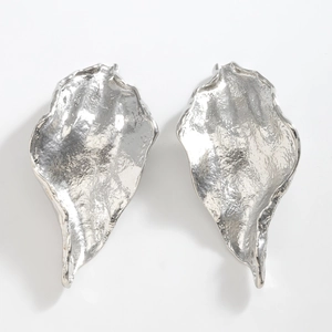 Macro detail of leaf-shaped silver earrings with textured hammered finish on metal surface