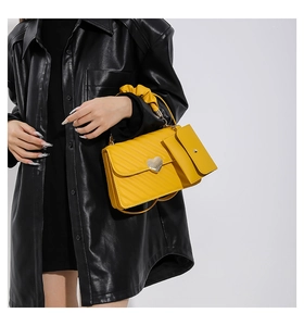 Detail of yellow crossbody bag featuring heart metal buckle and pleated handle with pouch