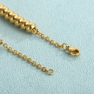 Macro detail of golden bead chain with lobster clasp and adjustable links on 18K gold plated steel