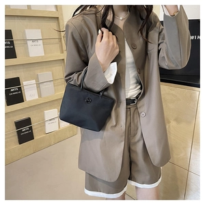 Détail d'un sac seau minimaliste en nylon noir porté avec un costume d'été kaki