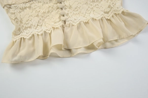 Detail of beige lace and chiffon top showing ruffled hem and fabric-covered buttons