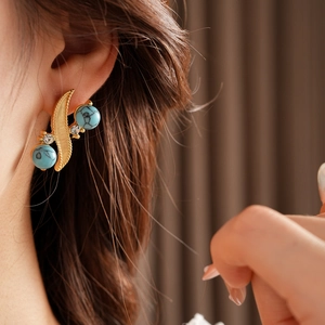 Detail of vintage gold leaf earring with turquoise beads and crystals on a model