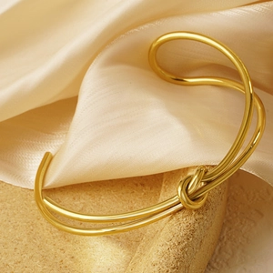 Minimalist 18K gold plated knotted open cuff bracelet on elegant silk and stone background