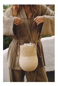 Detail of straw woven bucket bag with leather strap and drawstring lining on a model