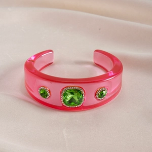 Detail of pink resin bangle featuring green gemstones and sparkling rhinestone accents