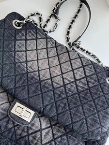 Macro shot of dark denim diamond quilted texture with silver chain strap and metal clasp