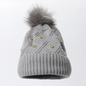 Bonnet en tricot gris avec grand pompon doux et clous de cœur dorés sur fond blanc