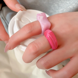 Close-up of pink marbled acrylic rings set on hand holding a white coffee cup