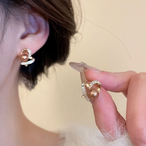 Detail of heart-shaped pearl earrings with gold plating and sparkling crystals on ear