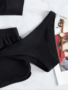 Flat lay of black sporty three-piece bikini set on white marble with fashion accessories