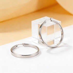 Minimalist silver stainless steel hoop earrings on white platform with yellow fabric background