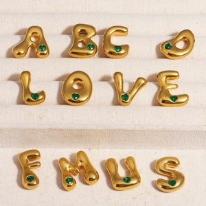 Détail de pendentifs lettres dorées avec cœurs verts sur doublure en velours beige