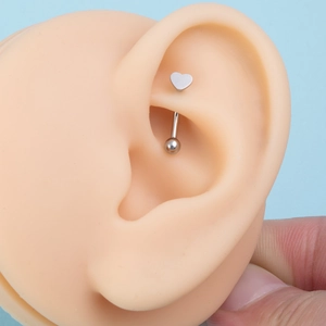 Close-up of heart-shaped stainless steel piercing stud on a silicone ear model