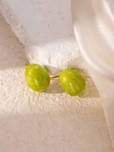 Macro shot of oval green marble earrings on white stone texture and silk fabric