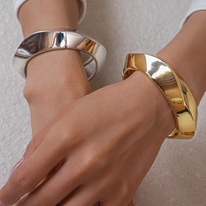 Close-up of chunky gold and silver geometric twisted metal bangles on model wrists