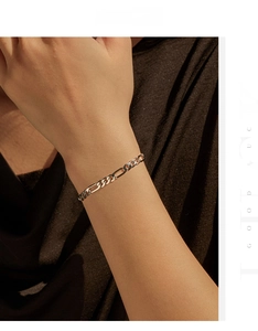 Detail of silver Figaro chain bracelet on wrist with warm vintage aesthetic lighting
