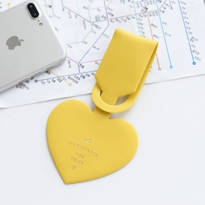 Detail of yellow heart-shaped leather luggage tag with litchi texture on a map background