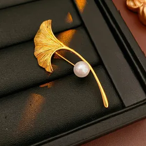 Elegant gold-plated ginkgo leaf brooch with a single white pearl on a black display base