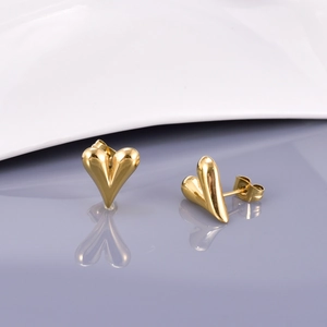 Détail des boucles d'oreilles cœur plaquées or 18K sur une surface réfléchissante grise