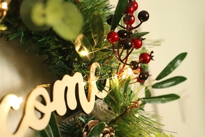 Close-up of LED Christmas wreath with pine cones, red berries and Welcome wooden sign
