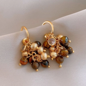 Close-up of golden tassel earrings with brown tiger eye beads and sparkling zircon stones