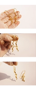 Detailed view of hand-held irregular wave-shaped gold earrings with artistic flowing lines