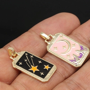 Macro detail of gold-plated Tarot pendants showing The Star and The Moon enamel designs