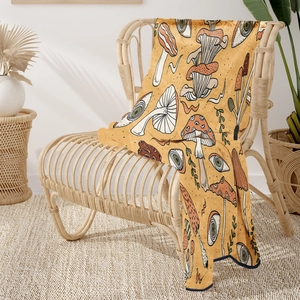 Detail of bohemian flannel blanket with mushroom and eye patterns on a rattan chair