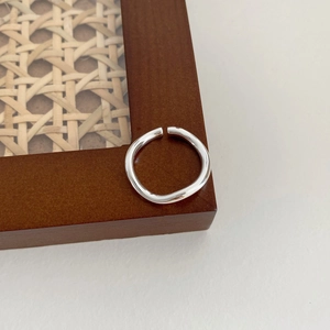 Close-up of silver hollow wave geometric open ring on a dark brown wooden frame edge